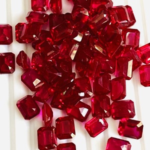 May include: A pile of loose, faceted, red ruby gemstones. The gemstones are all cut in a rectangular shape with sharp edges and corners.