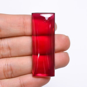 Könnte beinhalten: Ein rechteckiger, tief roter Cabochon-Edelstein mit einer glatten, polierten Oberfläche.
