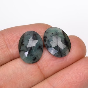May include: Two oval-shaped green gemstones with a faceted cut. The gemstones have a dark green colour with black inclusions.