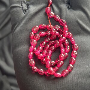 May include: A strand of pink oval-shaped beads, strung together with a thin red cord.