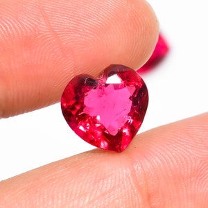 Puede incluir: Una piedra preciosa rosa brillante en forma de corazón con facetas. La piedra preciosa está tallada en forma de corazón y tiene un alto pulido.