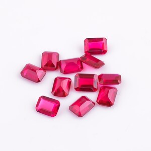 Könnte beinhalten: Zwölf rote Edelstein-Cabochons, in rechteckiger Form geschnitten, liegen verstreut auf einer weißen Oberfläche.