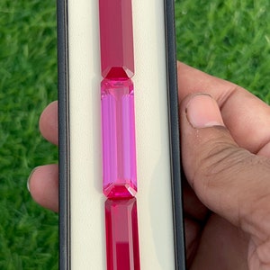 May include: Three rectangular gemstones in a white display box. The top and bottom gemstones are red, and the middle gemstone is a light pink and purple.