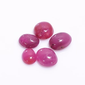 Peut inclure: Cinq pierres précieuses ovales polies de différentes nuances de rouge et de rose sont disposées sur une surface blanche. Les gemmes ont un aspect lisse et brillant, avec de subtiles variations de couleur et de motifs internes. Les pierres sont probablement des rubis.
