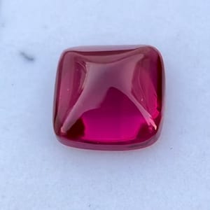 Könnte beinhalten: Ein quadratischer Edelstein in tiefroter Farbe mit einer polierten, facettierten Oberfläche.