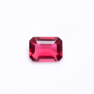 May include: A deep red, emerald-cut gemstone with a high polish.