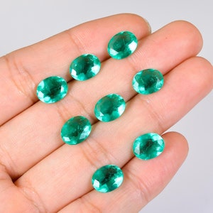 Op de afbeelding: Acht ovale, gefacetteerde, groene edelstenen. De edelstenen zijn in een halve cirkel op een hand gerangschikt.