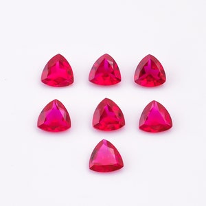 May include: Seven triangular red gemstones on a white background.