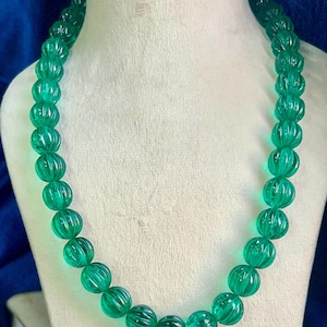 Op de afbeelding: Een groene glazen ketting met gefacetteerde kralen. De kralen zijn rond en hebben een geribbelde textuur.