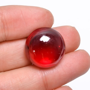 Puede incluir: Una piedra preciosa cabujón de color rojo intenso con una superficie lisa y pulida.