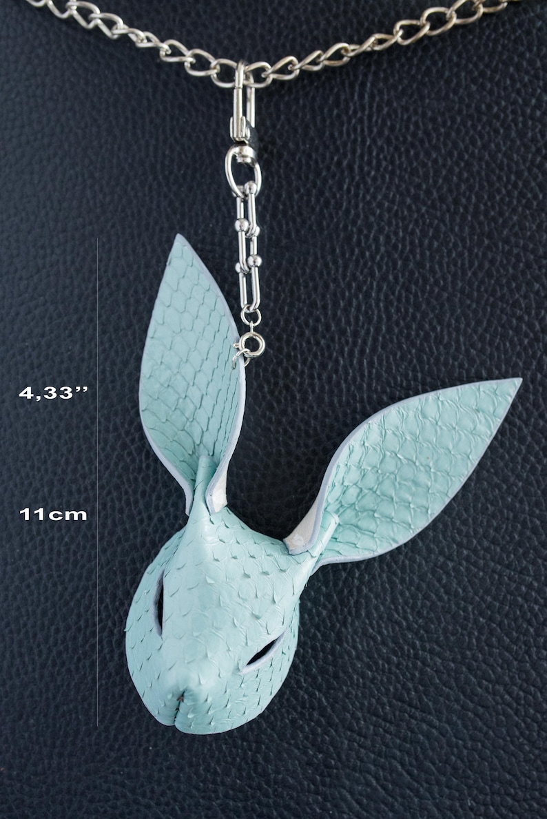 May include: A light blue leather bunny mask pendant with a silver chain. The mask is 11 cm long and features a textured, scale-like pattern. The pendant hangs from a silver chain.