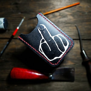 Könnte beinhalten: Schwarzer Lederkartenhalter mit einem weißen Mittelfinger-Design und roten Nähten.