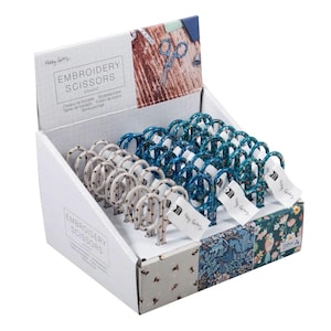 May include: A display box of embroidery scissors with patterned handles in blue and cream. The box is white and features the words "EMBROIDERY SCISSORS". The box has decorative floral patterns on the sides and base.