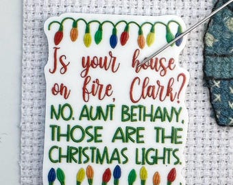 Może przedstawiać: Biała naklejka z napisem "Is your house on fire, Clark?" i "No. Aunt Bethany, those are the Christmas lights." Naklejka jest ozdobiona kolorowymi lampkami choinkowymi, idealna na święta.