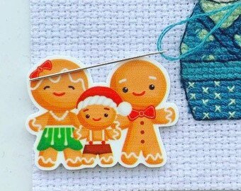 Może przedstawiać: Zestaw trzech ozdób piernikowych w kształcie ludzików: kobiety, mężczyzny i dziecka. Kobieta ma na sobie zieloną spódniczkę, mężczyzna czerwony krawat, a dziecko czerwoną czapkę Mikołaja.
