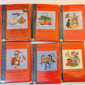 May include: Six cross-stitch kits in red packaging, each with a festive design. Designs include owls, a cat by a fireplace, and a van with a Christmas tree. Each kit includes a card and envelope, perfect for seasonal crafting.