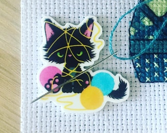 May include: A black cat with yellow yarn wrapped around it, sitting with a needle and yarn balls. The cat has green eyes and a pink nose. The yarn balls are pink, blue, and yellow.