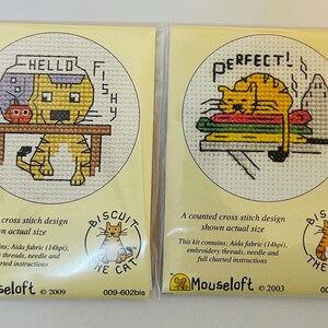 May include: Two cross-stitch kits featuring Biscuit the Cat. One shows a cat with a fishbowl, the text reads "HELLO FISHY". The other shows a cat on a stack of laundry, with the text "PERFECT!". Both kits include Aida fabric, embroidery threads, and instructions.