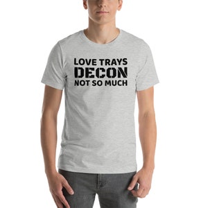 May include: A light gray t-shirt with the text "LOVE TRAYS DECON NOT SO MUCH" printed in black. The shirt is short-sleeved and has a crew neck.