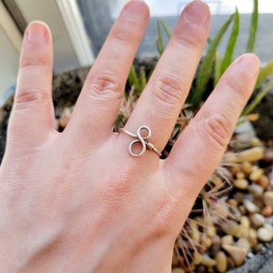 Può includere: Un anello in filo d'argento con un design a doppio anello. L'anello è impreziosito da un piccolo dettaglio in filo d'oro.