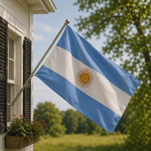 Pode incluir: A bandeira nacional da Argentina apresenta três faixas horizontais em azul claro e branco, com um emblema de sol dourado centralizado na faixa branca. A bandeira está montada em um mastro de metal fixado na lateral de um edifício branco.