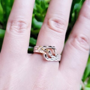 Può includere: Un anello d'argento con un design ondulato e testurizzato. L'anello è indossato su un dito.