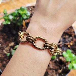 Op de afbeelding: Een gouden armband met een touwachtig kettingontwerp. De armband heeft grote, ovale schakels.
