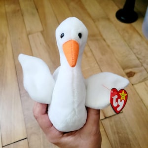 May include: White plush swan beanie baby with an orange beak and a red Ty heart tag with a white star.