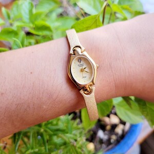 May include: A gold-tone wristwatch with a white face and a gold-tone band. The watch face has a diamond-shaped accent at the 12 o'clock position and the words "Remington Geneva" printed on it.