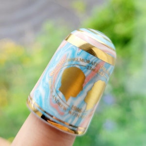 May include: A blue and pink thimble with gold trim commemorating the wedding of Prince Andrew and Sarah Ferguson on July 23, 1986. The thimble features a silhouette of the couple.
