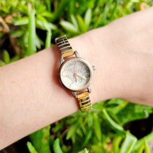 May include: A gold-toned watch with a white face and a world map design. The watch has a metal band.