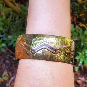 Puede incluir: Un brazalete de puño de latón martillado con un diseño en zigzag de metal negro.