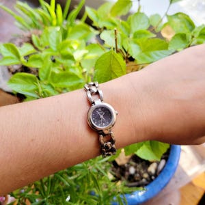 May include: A silver wristwatch with a black face and silver band. The watch is on a person's wrist.