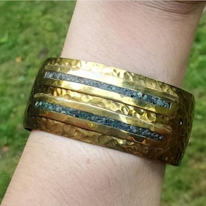 Puede incluir: Un brazalete de metal martillado en tono dorado con tres bandas incrustadas de piedra verde oscura.