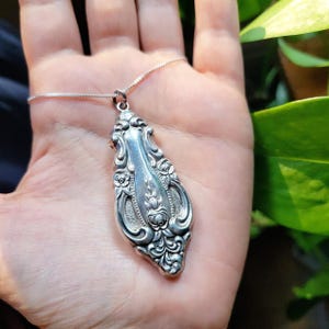 May include: A silver necklace with a detailed pendant shaped like a teardrop. The pendant has a floral design with intricate details.
