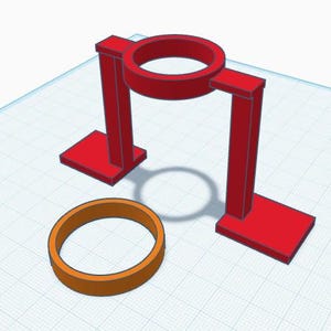May include: A 3D-rendered image of a red stand with a circular top and base, and an orange ring. The stand has a rectangular base and two vertical supports. The orange ring is on the surface below the stand.
