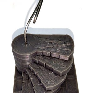 Può includere: Una miniatura di scala a chiocciola stampata in 3D, grigio scuro, con un accento metallico. La scala è composta da gradini curvi a strati e una piattaforma circolare. La base è una griglia di quadrati. L'accento metallico è curvo.