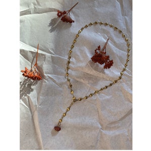 Könnte beinhalten: Eine goldene Halskette mit herzförmigen Gliedern und einem roten Herz-Anhänger. Die Kette liegt auf einem weißen, strukturierten Hintergrund.