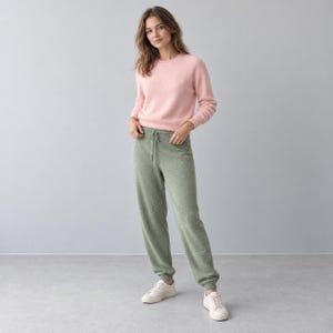 Op de afbeelding: Een lichtroze trui met lange mouwen en ronde hals gecombineerd met een saliegroene gebreide joggingbroek met trekkoord in de taille en geribbelde boorden, gedragen met witte vetersneakers. De outfit bestaat uit een zachte gebreide top en broek.