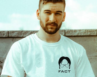 Może przedstawiać: Biały t-shirt z czarnym nadrukiem przedstawiającym mężczyznę w okularach i napisem "FACT" pod spodem.