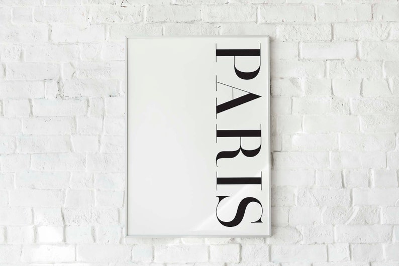K&ouml;nnte beinhalten: Ein wei&szlig;er gerahmter Poster mit dem Wort "PARIS" in schwarzen vertikalen Buchstaben.
