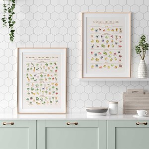 Puede incluir: Dos impresiones enmarcadas, "Gu&iacute;a de verduras de temporada" y "Gu&iacute;a de frutas de temporada", expuestas en una estanter&iacute;a blanca. Las gu&iacute;as presentan ilustraciones coloridas de varias frutas y verduras. Los marcos tienen un acabado de madera clara. La cocina tiene gabinetes verde menta y un salpicadero de azulejos hexagonales blancos.