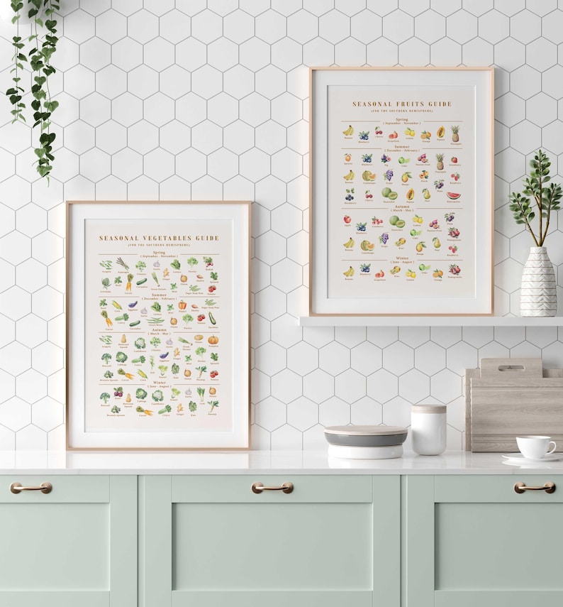 Puede incluir: Dos impresiones enmarcadas, "Gu&iacute;a de verduras de temporada" y "Gu&iacute;a de frutas de temporada", expuestas en una estanter&iacute;a blanca. Las gu&iacute;as presentan ilustraciones coloridas de varias frutas y verduras. Los marcos tienen un acabado de madera clara. La cocina tiene gabinetes verde menta y un salpicadero de azulejos hexagonales blancos.