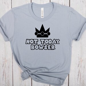 Puede incluir: Una camiseta azul claro con un gr&aacute;fico negro de una corona y el texto "Not Today Bowser".
