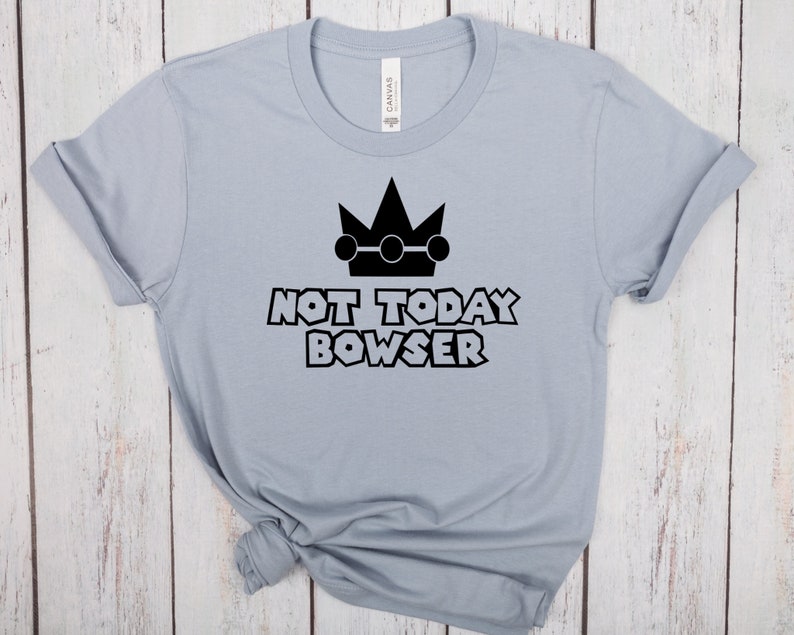 Puede incluir: Una camiseta azul claro con un gr&aacute;fico negro de una corona y el texto "Not Today Bowser".