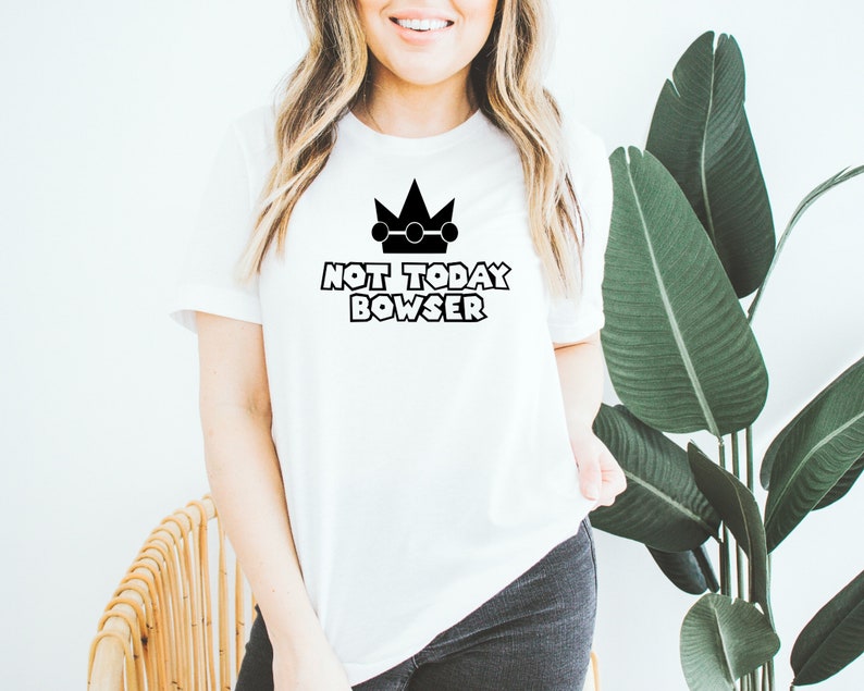 Puede incluir: Camiseta blanca con una corona negra y el texto "NOT TODAY BOWSER".