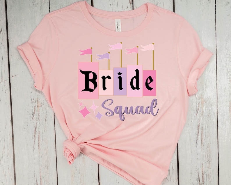 May include: Pink t-shirt with a castle graphic and the text "Bride Squad" in black.