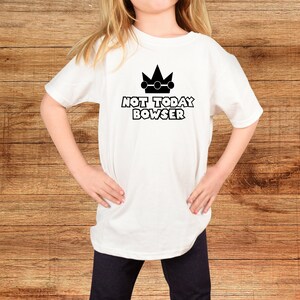 Puede incluir: Camiseta blanca con una corona negra y el texto "NOT TODAY BOWSER" impreso en la parte delantera.