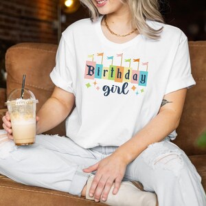 Peut inclure: Un t-shirt blanc avec un motif color&eacute; qui dit "Birthday girl" avec des drapeaux et des &eacute;toiles autour du texte.
