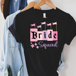 May include: Black t-shirt with a pink and purple castle graphic and the text "Bride Squad".